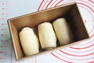 再次擀开成长条状，面团卷起，收口朝下放置，将面团放入吐司模。