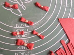 将红色小面团擀平擀簿，切成细长条，然后弄成蝴蝶结。