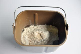 把液体材料放入面包桶中，面粉铺在上面，对角分别上放上盐、糖、奶粉，在面粉中间挖一个小坑，放上酵母，启动面包机揉面程序10分钟。