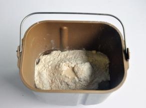 把液体材料放入面包桶中，面粉铺在上面，对角分别上放上盐、糖、奶粉，在面粉中间挖一个小坑，放上酵母，启动面包机揉面程序10分钟。