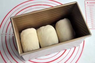 再次擀开成长条状，面团卷起，收口朝下放置，将面团放入吐司模。