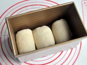 再次擀开成长条状，面团卷起，收口朝下放置，将面团放入吐司模。