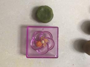 取一个绿茶味桃山皮，包上馅料，再取一个花型模具，在中间放上白色桃山皮圆球，梅花型状上放上桔色，花蕾上放上原色台山皮，边上清理干净。以下方法同上