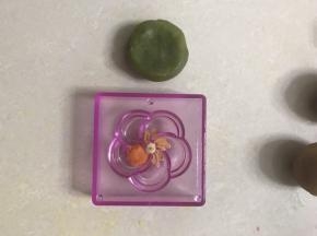取一个绿茶味桃山皮，包上馅料，再取一个花型模具，在中间放上白色桃山皮圆球，梅花型状上放上桔色，花蕾上放上原色台山皮，边上清理干净。以下方法同上