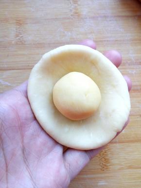 取一块水油皮，擀成圆饼，把油酥像包包子一样包住，封口朝下