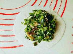 取一小块面团用擀面杖擀圆饼，包上韭菜鸡蛋馅。