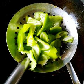 把青椒块放在漏勺中，另一只手拿勺子舀油来浇，青椒皮起泡即可。