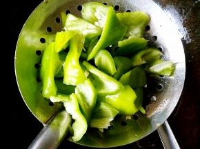 把青椒块放在漏勺中，另一只手拿勺子舀油来浇，青椒皮起泡即可。