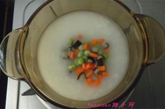 取一碗煮好的大米粥，倒入小锅里，放入豌豆粒、胡萝卜丁和香菇丁，搅拌匀煮一分钟；