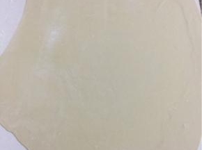 案板上撒少许面粉，面团用擀面杖擀成薄片。

