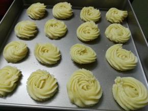 将曲奇面糊挤入烤盘，我用的是学厨金盘，不用垫油纸，挤曲奇时注意裱花嘴应与烤盘垂直朝下，停顿一下、慢慢转圈、慢慢收尾，收尾时也要停顿一下，这样挤出来的曲奇花比较好看；注意一盘曲奇挤的大小一致、曲奇之间要留点空隙。