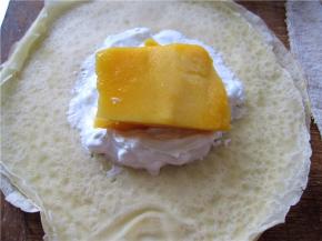 摊开一张面皮，表面光滑的那一面朝下。取适量打发好的奶油放在面皮中间。放上一块条状的芒果。我切的有点大哟，舍不得切掉呢，呵呵。