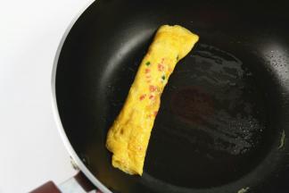 待鸡蛋液凝固后，用铲子挑起蛋饼的一边，卷成鸡蛋卷，挪到锅一边。