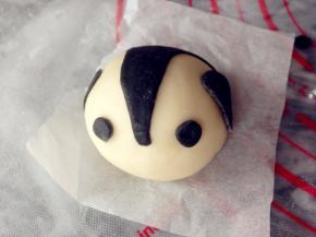 将馒头坯揉圆，放在油纸上，摆放在蒸笼里。做一个才取出来一个，将黑色的梯形面皮拉长，从圆形中间部分一直向后拉。贴上眼睛，两边贴上前肢。如图摆放好，可以在沾一点点水，贴得更牢固