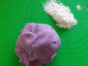 揉面结束后，取出面团，紫薯泥面团比白色面团稀点，准备点手粉进行下面的操作