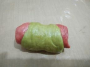 三个红曲粉面皮两个抹茶面皮叠加从上而下卷起，用刀在中间切开