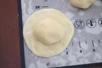 取一块水油皮面团，用手掌按扁，中间略厚，边缘稍薄，水油面团中间放一个油酥面团