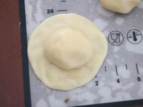 取一块水油皮面团，用手掌按扁，中间略厚，边缘稍薄，水油面团中间放一个油酥面团