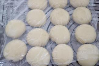 放在虎口位置，一边转一边将面团慢慢向上收口，捏紧并收口，面团收口朝下，整成圆球状，全部包好后，盖上保鲜膜，静置松弛20分钟