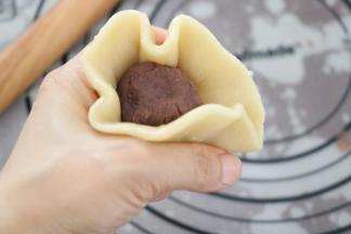 饼皮放在虎口位置，放一颗豆沙馅，右手压住内馅，左手一边转一边收口