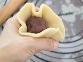 饼皮放在虎口位置，放一颗豆沙馅，右手压住内馅，左手一边转一边收口