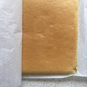 烤好的蛋糕取出，在桌上轻磕一下震出热气，顺着油纸提出蛋糕，稍微凉一下撕去油纸，然后再盖上油纸以免干燥，等待蛋糕放凉