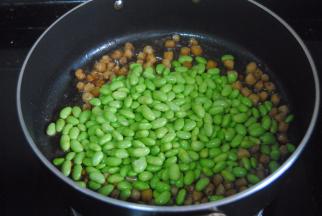 .这时倒入毛豆翻炒均匀，加入刚浸泡干贝的清水，翻匀后焖煮片刻