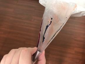 制作马卡龙。先将中号圆形花嘴放入裱花袋，用牙签粘点色素，沿着裱花袋拉一条线。你想做什么颜色就拉几条。