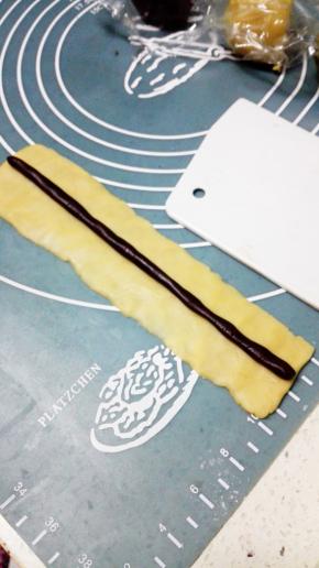 取25克原味面团，搓成长条后压扁，约长15cm宽5cm的长方形，再取4克可可面团，搓成15cm的圆长条，放在原味面团上，完成熊猫的鼻子部分