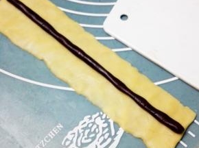 取25克原味面团，搓成长条后压扁，约长15cm宽5cm的长方形，再取4克可可面团，搓成15cm的圆长条，放在原味面团上，完成熊猫的鼻子部分