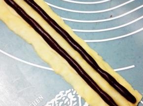 取两个各7克的可可面团，分别搓成15cm的长圆条放在鼻子的两侧，这是熊猫的眼睛