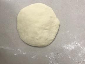 取一个面团用手掌压扁，边上稍薄，边上的气泡尽量用手拍了。