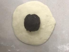  放上红豆沙，象包包子那样慢慢收口，捏紧收口收口朝下，用二手撑来回搓圆，放入烤盘整好型。