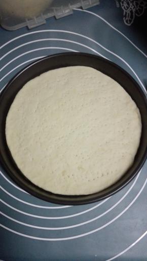 将静置后的一个面团擀成薄饼状，约披萨盘大小，放入披萨盘，用叉子在上面轻按出小孔