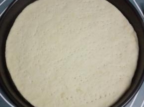 将静置后的一个面团擀成薄饼状，约披萨盘大小，放入披萨盘，用叉子在上面轻按出小孔