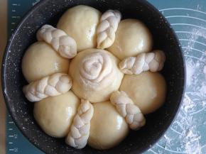 将做好的长辫子，中间切一刀分成两段，共成为6条短辫子，头尾都要捏紧，表面洒上面粉，放在两个面包坯中间，在大的面包坯中间放入玫瑰花，玫瑰花面包坯也要洒上面粉。