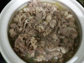 把烫熟的羊肉卷连同汤汁一起倒入盛有酸菜金针茹的砂锅中。