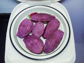  将紫薯清洗干净，对半切开，放入电饭煲中选择蒸煮建蒸熟