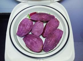  将紫薯清洗干净，对半切开，放入电饭煲中选择蒸煮建蒸熟