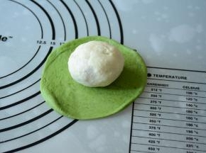 将包好的白色面团放在绿色面皮中间。