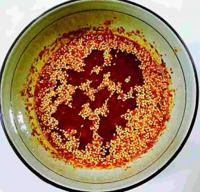 倒入三分之一的油，边倒油边搅拌，然后油在稍稍加热一下，再倒入三分之一，最后将剩下的油在烧热一下，倒入辣椒油中，紧接着放入花生碎，熟芝麻，搅拌均匀