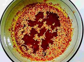 倒入三分之一的油，边倒油边搅拌，然后油在稍稍加热一下，再倒入三分之一，最后将剩下的油在烧热一下，倒入辣椒油中，紧接着放入花生碎，熟芝麻，搅拌均匀