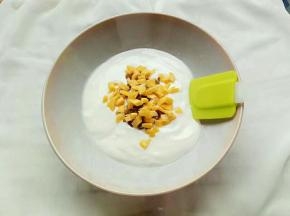 再将酸奶倒入碗中，依次把葡萄干和芒果干碎放入碗中