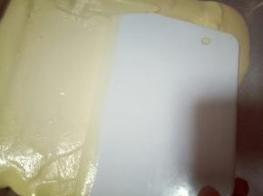 用刮板将蛋糕糊刮平，烤盘垂直震几下，震出气泡。