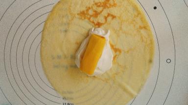 取一张面皮，取朝锅底面朝上，放一大勺奶油，奶油上再放一块芒果