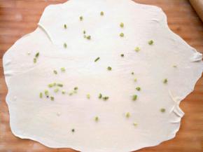 取一团面撒上手粉防止粘，擀成薄薄的面片，抹上油酥，撒上葱花，卷起来