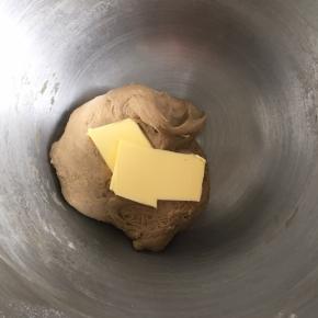 把面团揉成摸上去有点粘，但是不会粘到面团在手上的状态，加入软化的黄油，继续揉面