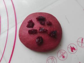 取一红色面团压扁，加入少量切碎的蔓越莓。