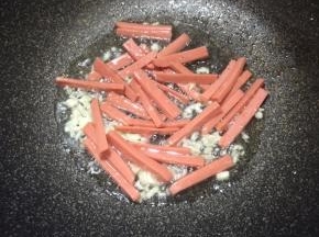 下入火腿肠煸至表面微焦。