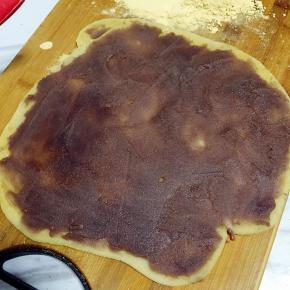 在面板上和面团上撒上少许炒熟的黄豆面，用擀面杖擀成方形，均匀抹上豆沙馅；